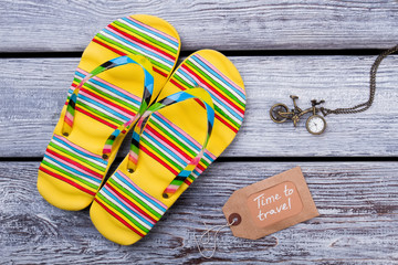 Time to travel concept. Sandals flip flops and clock on wooden desk surface background. Flat lay,...