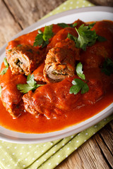 Italian meat roll braciole stuffed with parsley and cheese in tomato sauce close-up. vertical