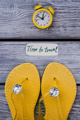 Yellow luxury footwear and alarm clock. Time to travel. Dark wooden surface background.