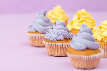 Cupcakes decorated with yellow and violet cream decorations on pastel background.