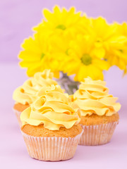 Cupcakes decorated with yellow cream and chrysanthemums on violet pastel background.
