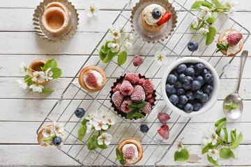 Close-up photo of homemade cakes with mascarpone cheese, cinnamon, frozen raspberries,  mint, blueberries and beautiful wild apple tree flowering branches. Top view on white vintage wood background