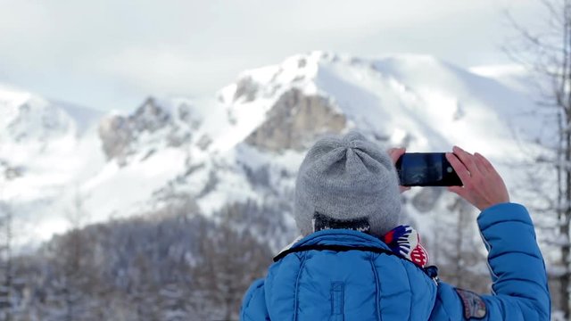 Young woman uses a smartphone to video a beautiful view in the snowy mountains, rear view
