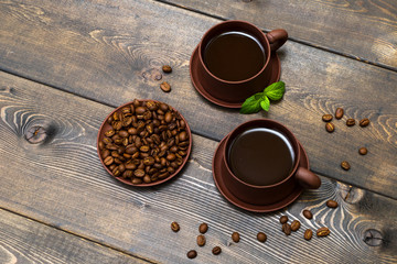 Coffee or chocolate in clay mugs on a background of a wooden table of dark color. A leaf of mint and a grain of coffee.