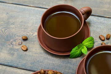 Coffee or chocolate in clay mugs on a background of a wooden table of dark color. A leaf of mint and a grain of coffee.