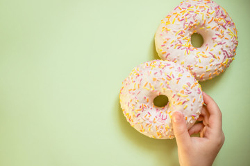 Sweet tasty snack. kids hand hold glazed donut on green background ,top view, copy space.Unhealthy food concept.classic two glazed donuts isolated.Delicious colorful donuts