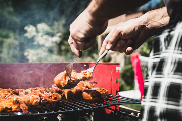 Fototapeta premium Pulling the chicken on the grill. The man pulls the finished chicken legs on the grill. Spending time together with the family at the grill. Social meetings, friends. Red gril with kindling and coal.