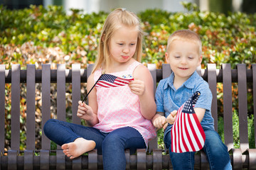 Fototapeta premium Young Sister and Brother Comparing Each Others American Flag Size On The Bench At The Park