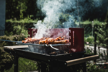 Grill view with chickens. Chickens and sausages are fried on the grill. Spending time together with the family at the grill. Social meetings, friends. Red gril with kindling and coal.