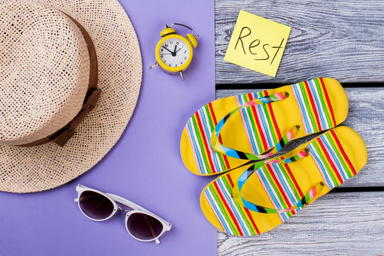 Rest and resort concept flat lay. Straw hat, alarm clock, sunglasses and flip-flops.