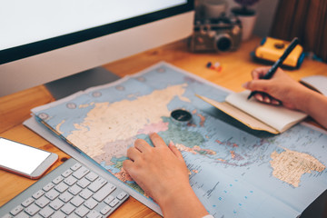Beautiful young planning travel trip. Workspace with computer,map,notebook,snack and phone on...