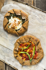 Summer galette with tomatoes, pepper, spinach, feta, cheese, tofu and salt vegetarian dough on wooden desk. Summer food, summer pie on parchment paper, open pie, process of baking