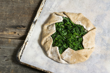 Summer galette with tomatoes, pepper, spinach, feta, cheese, tofu and salt vegetarian dough on wooden desk. Summer food, summer pie on parchment paper, open pie, process of baking, raw dought.