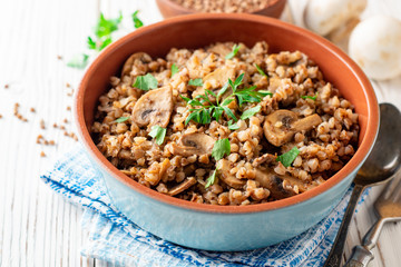 Buckwheat porridge with mushrooms in a bowl on white wooden background