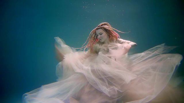 a young woman shows up at the hem of a dress that flutters under the water, the atya in which she is dressed, the lady seems mystical and frightening with dreadlocks on her head