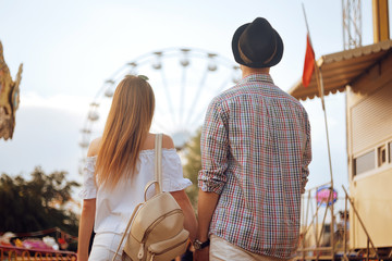 Beautiful, young couple having fun at an amusement park. Couple Dating Relaxation Love Theme Park Concept. Couple posing together on the background of a ferris wheel. Tourists have fun, smile