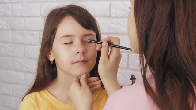 Makeup to the child. To the little girl, the older sister makes an eye makeup.