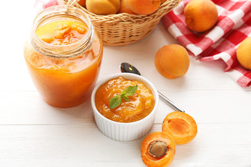 Apricot jam in bowl and glass jar on white wooden table