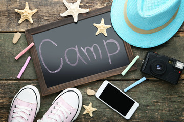Inscription Camp with smartphone, retro camera and clothes on wooden table