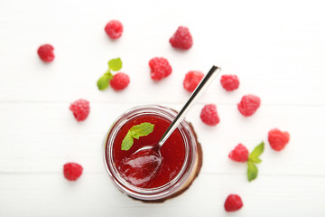 Raspberry jam in glass jar with spoon on wooden table