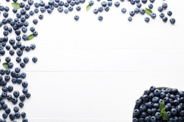 Ripe blueberries with green leafs on white wooden table
