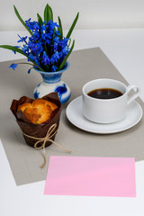 Cupcake Muffin and a cup of coffee, blue spring flowers. A pink sheet of paper. Copy space.