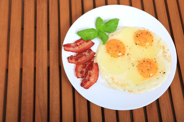 Jajko sadzone na białym talerzu z boczkiem i bazylą. © Stanisław Błachowicz