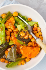 Salad with baked pumpkin and chickpeas with mustard-honey dressing in a white plate, top view. Healthy vegan food concept.