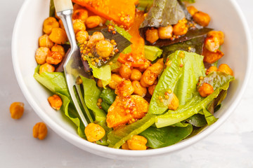 Salad with baked pumpkin and chickpeas with mustard-honey dressing in a white plate, macro. Healthy vegan food concept.
