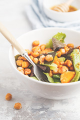 Salad with baked pumpkin and chickpeas with mustard-honey dressing in a white plate, macro. Healthy vegan food concept.