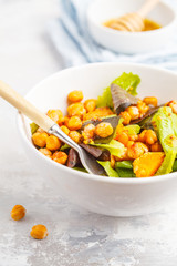 Salad with baked pumpkin and chickpeas with mustard-honey dressing in a white plate, macro. Healthy vegan food concept.
