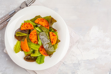 Salad with baked pumpkin in a white plate, copy space, top view. Healthy vegan food concept.