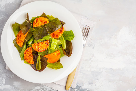 Salad with baked pumpkin in a white plate, copy space, top view. Healthy vegan food concept.