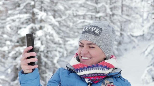 Young woman taking a self portrait with her smartphone in the snowy forest, Alps, Austria 