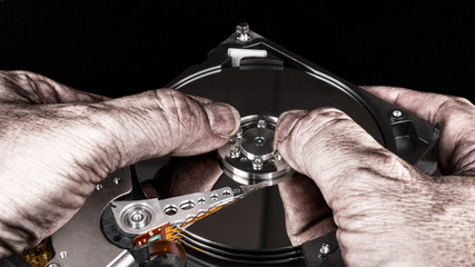 Dirty hands on hard disk drive. Artistic close-up, mirroring, black background. Computer spy with...