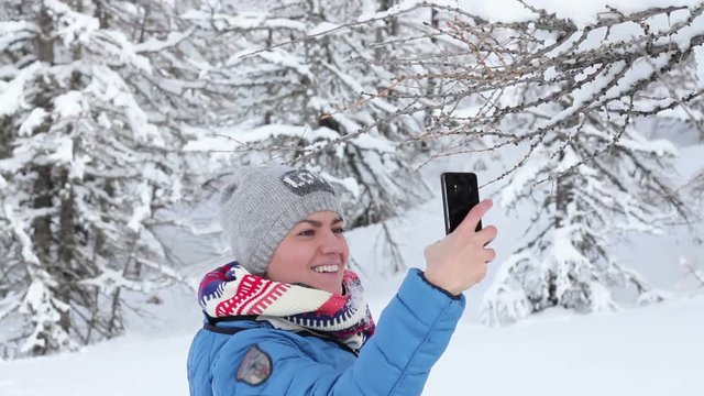 Young woman taking a self portrait with her smartphone in the snowy forest, Alps, Austria 