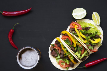 Tacos with beef and vegetables, beer and lime on a black background, top view. Mexican kitchen....