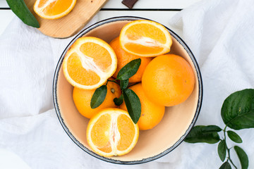 Juicy and fresh oranges with leaves  in bowl on white wooden table. Eye bird view 