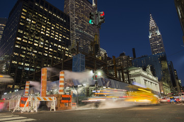Long exposure photo of cars crossing an intersection in New York City while steam coming out from the manhole. Empire State building in the background, Manhattan, USA.