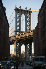 Brooklyn bridge seen from a narrow alley enclosed by two brick buildings during the sunset. New York City, USA.