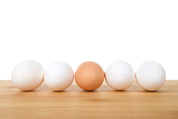 One speckled brown egg in the middle of four white eggs on a wood table with white background. Diversity concept. Copy space.