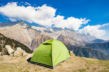 A single green tent seen against Dhaulahaar peaks of Himalayas in Triund. Sunny day whit some clouds. Dharamshala, Himachal Pradesh. India