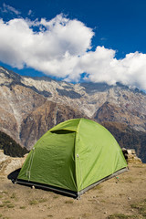 A single green tent seen against Dhaulahaar peaks of Himalayas in Triund. Sunny day whit some clouds. Dharamshala, Himachal Pradesh. India