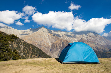 A single blue tent seen against Dhaulahaar peaks of Himalayas in Triund. Sunny day whit some clouds. Dharamshala, Himachal Pradesh. India