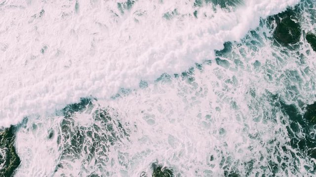 Abstract aerial view of moody ocean waves crashing on rocky shoreline 
