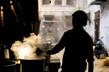 Silhouette of an Indian man preparing the famous Masala Chai. The Masala Chai is a flavoured tea beverage made by brewing black tea with a mixture of aromatic Indian spices and herbs