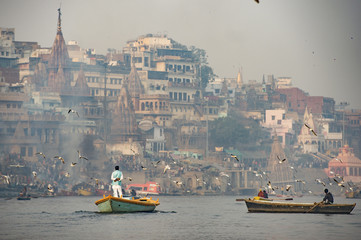 A man is sailing on his wooden boat in the sacred river Ganges in the city of Varanasi at sunset....