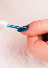 Detail of applying dark blue nail polis on the thumb
