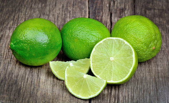 Lime slice and green limes on wooden background