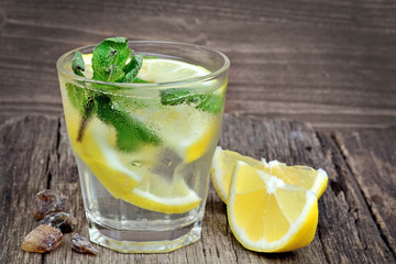 Water with lemon and mint in a glass on wood background